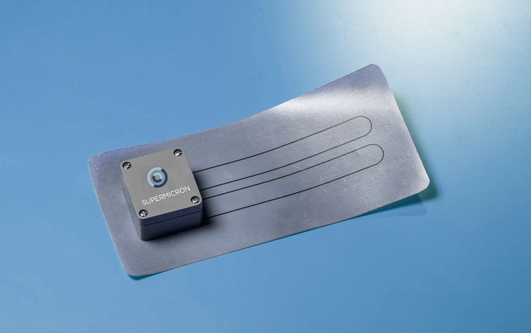 Sensore SuperMicron da studio: unità di acquisizione collegata a una striscia sensibile Smart Skin Sensor distesa, con le piste conduttive in evidenza, su fondo blu.